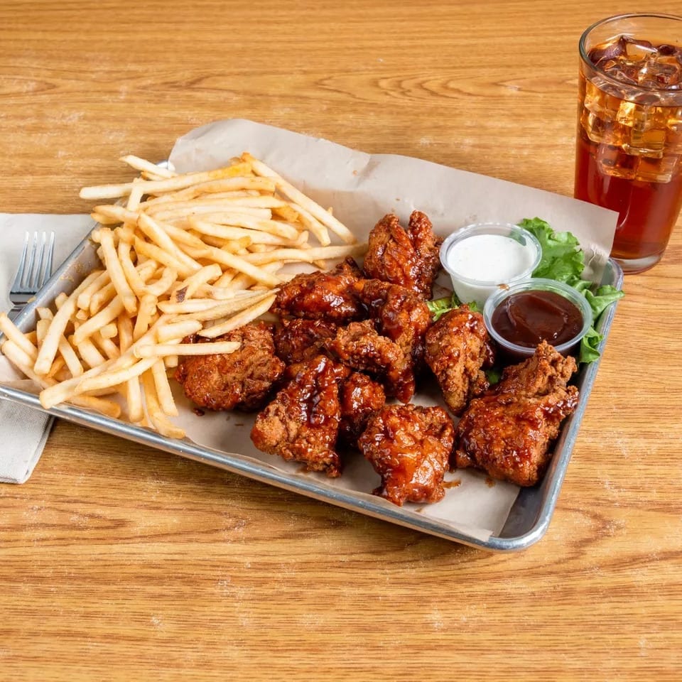 Crispy chicken wings with fries, dipping sauces, and a glass of iced tea on a wooden table.