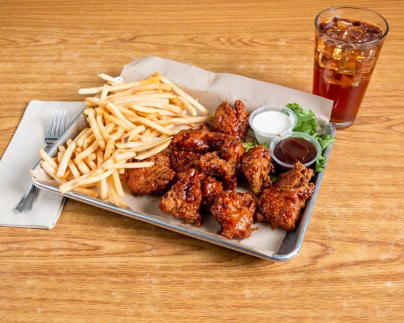 Crispy chicken wings with fries, dipping sauces, and a glass of iced tea on a wooden table.