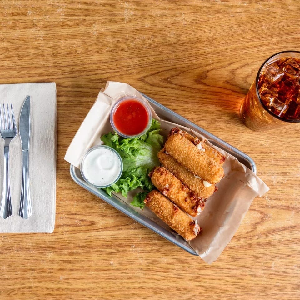Fried mozzarella sticks with dipping sauces, lettuce, and a drink on a wooden table.