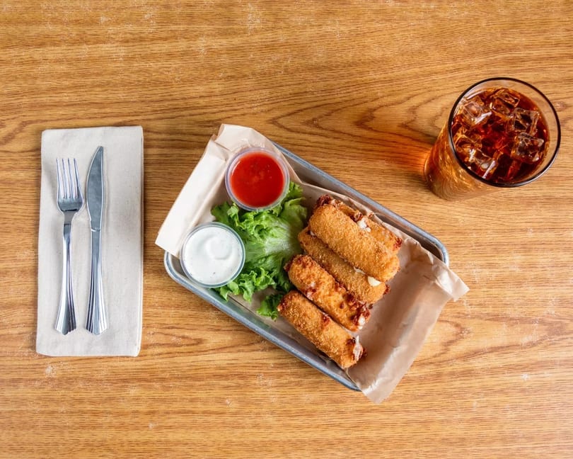Fried mozzarella sticks with dipping sauces, lettuce, and a drink on a wooden table.