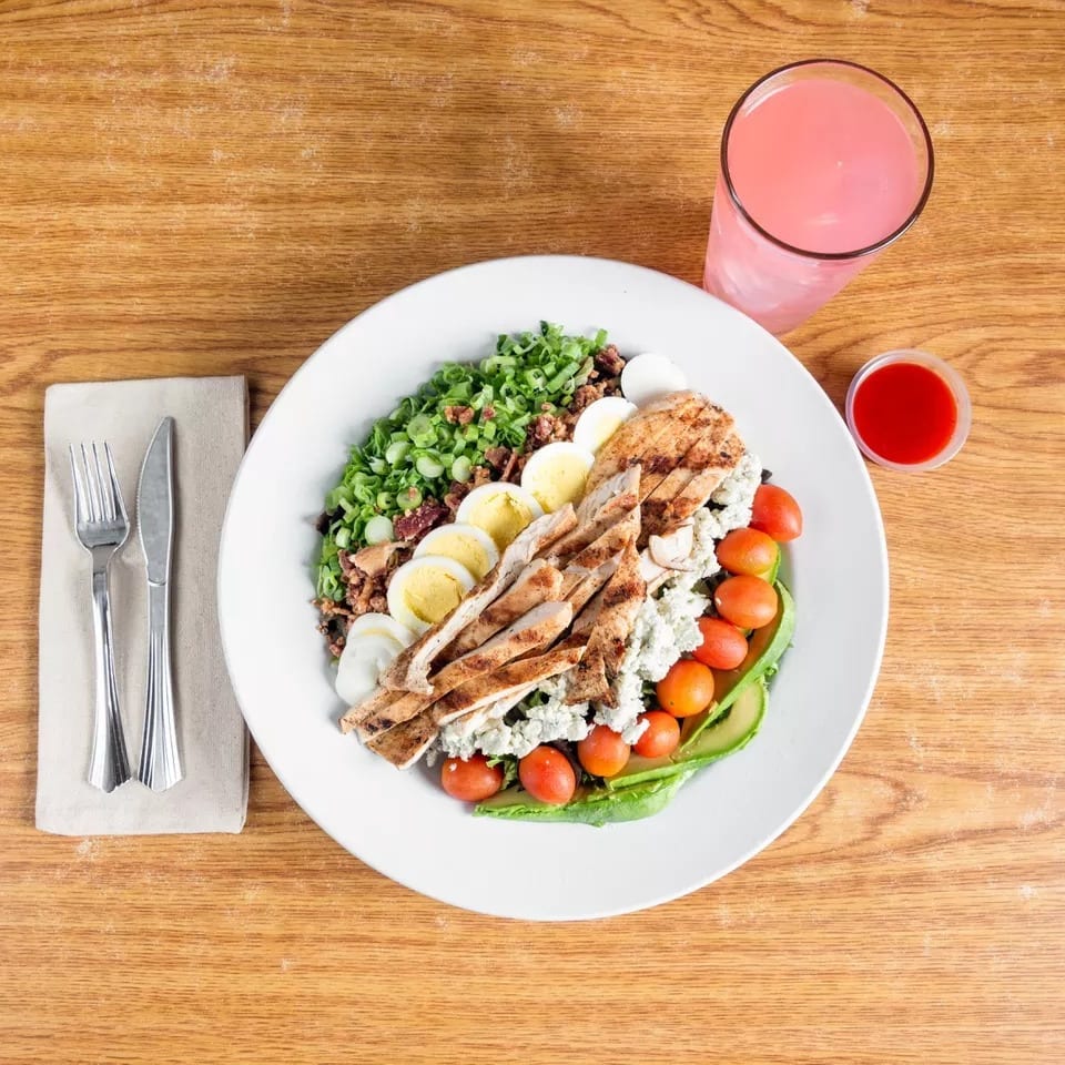 Cobb salad with grilled chicken, eggs, tomatoes, avocado, and blue cheese, with pink lemonade.