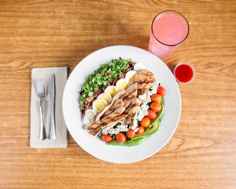 Cobb salad with grilled chicken, eggs, tomatoes, avocado, and blue cheese, with pink lemonade.