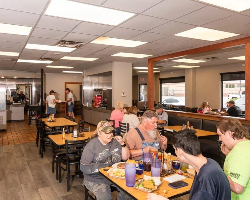 Diners enjoying meals at tables and booths in a brightly lit, casual restaurant interior.