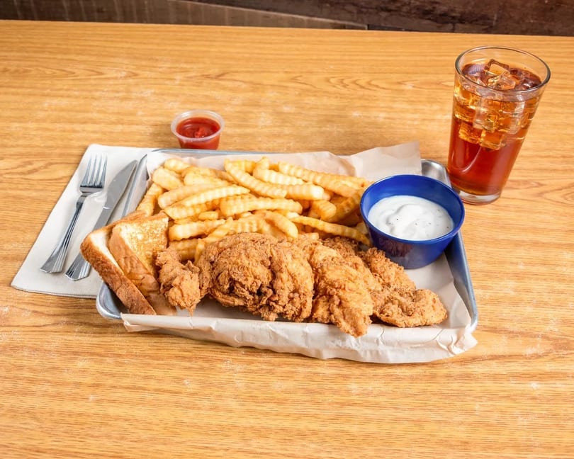 Fried chicken tenders, crinkle-cut fries, Texas toast, and dipping sauces on a tray with iced tea.