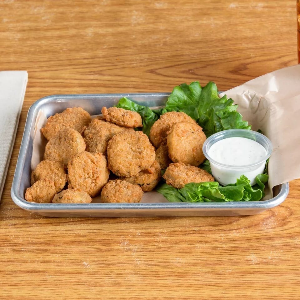 Fried pickles with lettuce and ranch dressing in a metal tray on a wooden table.