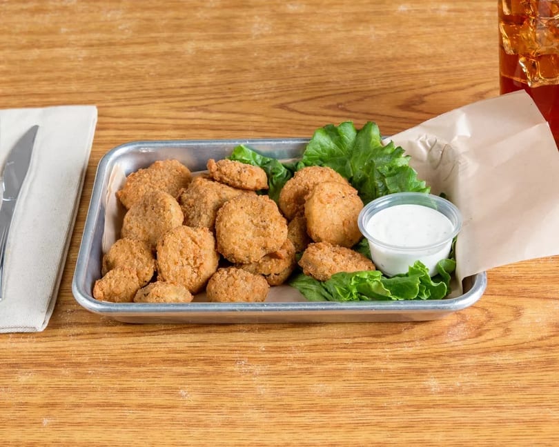 Fried pickles with lettuce and ranch dressing in a metal tray on a wooden table.