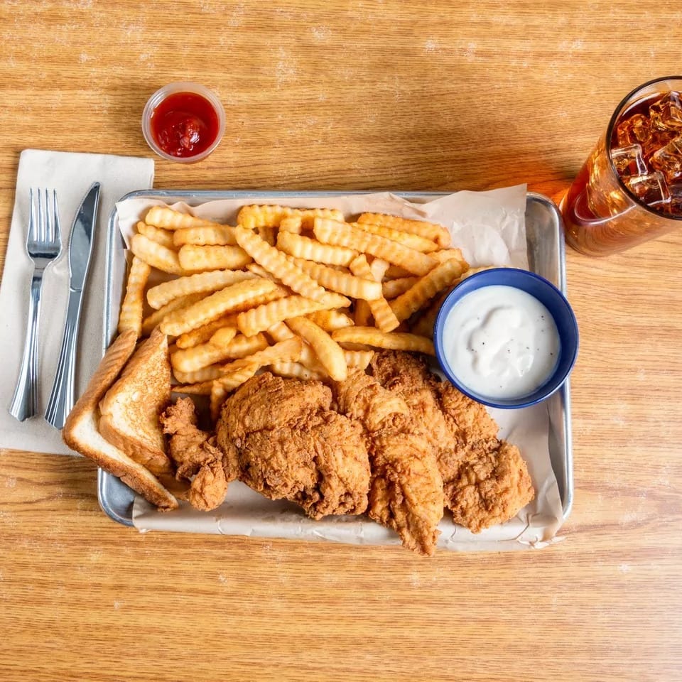 Fried chicken tenders, crinkle-cut fries, Texas toast, dipping sauces, and iced tea on a tray.