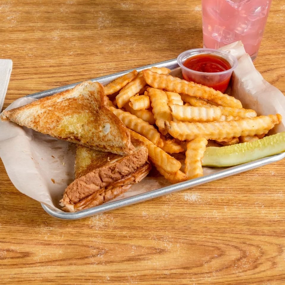 Grilled cheese sandwich with crinkle-cut fries, ketchup, and a pickle spear on a metal tray.