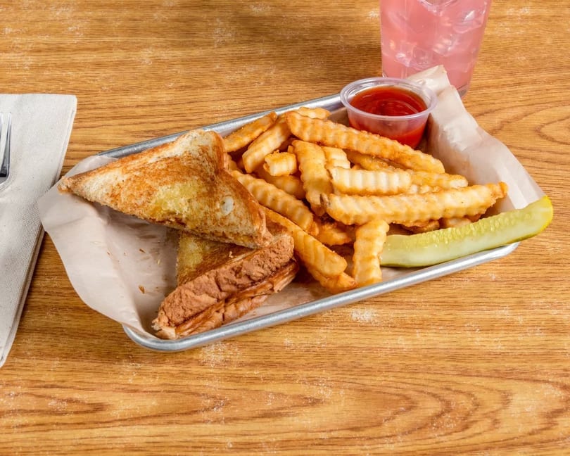 Grilled cheese sandwich with crinkle-cut fries, ketchup, and a pickle spear on a metal tray.
