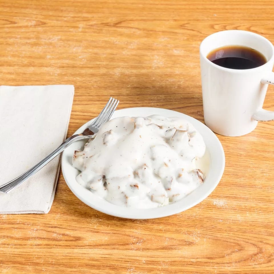 Biscuits and gravy with a fork on a napkin and a cup of coffee on a wooden table.