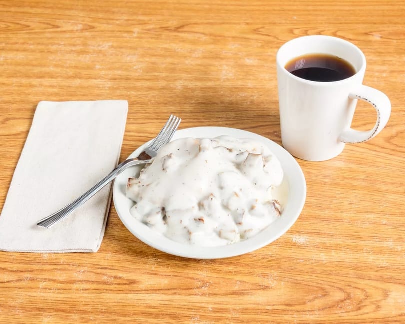 Biscuits and gravy with a fork on a napkin and a cup of coffee on a wooden table.