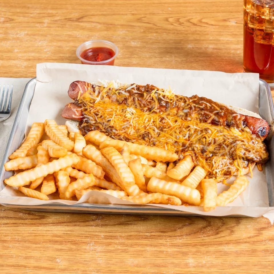Two chili cheese dogs with crinkle-cut fries, ketchup, and iced tea on a metal tray.