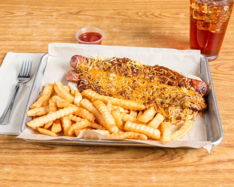 Two chili cheese dogs with crinkle-cut fries, ketchup, and iced tea on a metal tray.