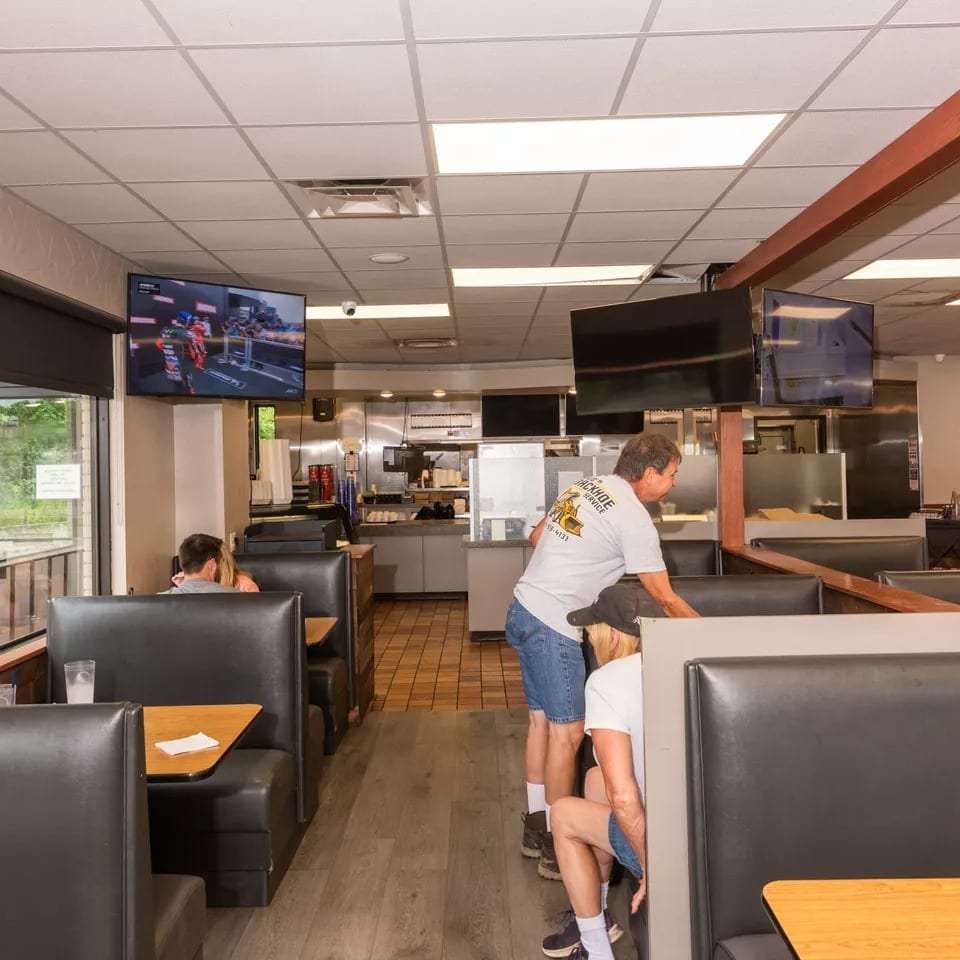 Restaurant interior with black booths, TVs, and staff working near the kitchen area.