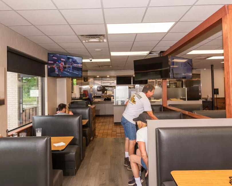 Restaurant interior with black booths, TVs, and staff working near the kitchen area.